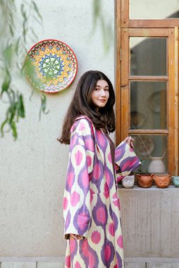 Güzel bir kadın, manken, Özbekistan moda elbisesi giymiş bir kız pencerenin yanında duruyor. Taşkent, Özbekistan