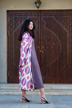 Güzel bir manken, geleneksel Özbekistan moda elbisesi giymiş ahşap kapılı bir kız. Taşkent, Özbekistan
