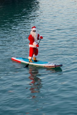 Santa in sunglasses stand on paddle board. Christmas, New Year clipart