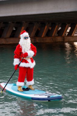 Güneş gözlüklü Noel Baba kürek tahtasında duruyor. Noel, Yeni Yıl