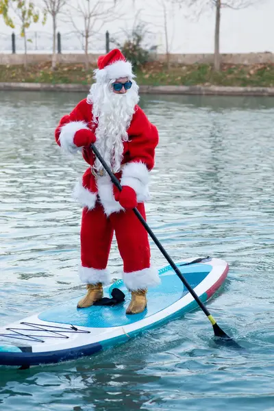 Güneş gözlüklü Noel Baba kürek tahtasında duruyor. Noel, Yeni Yıl