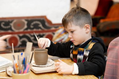 Bir çocuk çömlek atölyesinde demlik yapıyor.