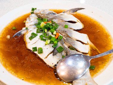 Beyaz tabakta servis edilen baharatlı soya soslu ve zencefilli Dory fileto balığı..