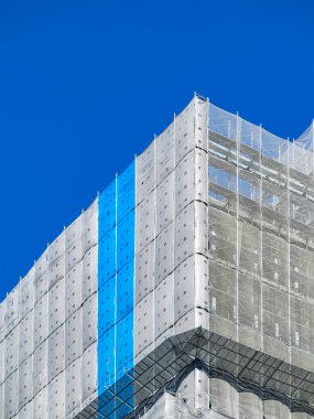 İnşaat halindeki bina mavi ve beyaz koruma ağı ile çevrili.