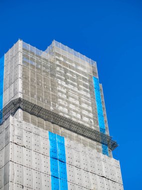 İnşaat halindeki bina mavi ve beyaz koruma ağı ile çevrili.