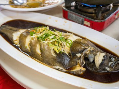 Soya soslu haşlanmış balık, beyaz tabakta servis edilir.