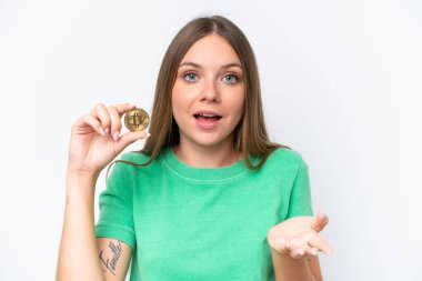Genç, sarışın bir kadın Bitcoin tutuyor beyaz arka planda izole edilmiş ve şok olmuş bir yüz ifadesi var.