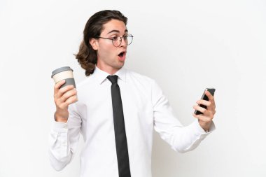 Beyaz arka planda izole edilmiş yakışıklı bir iş adamı elinde kahve ve bir cep telefonu tutuyor.