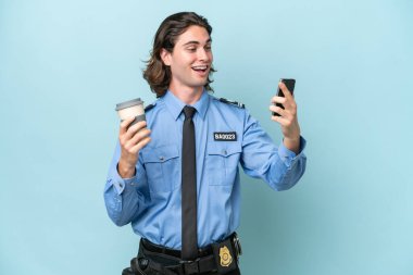 Kafkasyalı genç bir adam mavi arka planda izole edilmiş. Elinde kahve ve cep telefonu var.