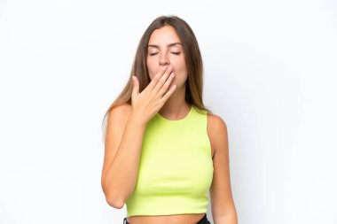 Beyaz arka planda izole edilmiş genç beyaz bir kadın esniyor ve geniş bir ağzı eliyle kapatıyor.