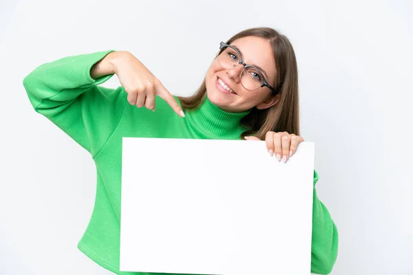 年轻的高加索女人 背景是白色的 手里拿着一张空空的标语牌 脸上带着快乐的表情 指着上面 — 图库照片