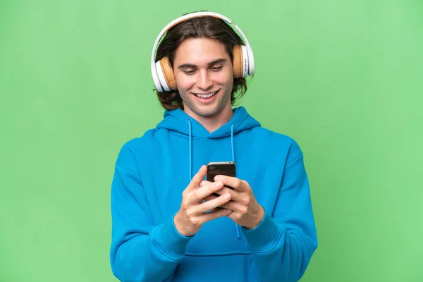 Νεαρός Όμορφος Άνδρας Απομονωμένος Στο Πράσινο Chroma Φόντο Ακούγοντας Μουσική — Φωτογραφία Αρχείου