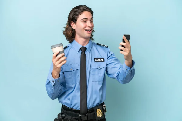 Молодой Кавказский Полицейский Изолированный Синем Фоне Кофе Мобильным Телефоном — стоковое фото
