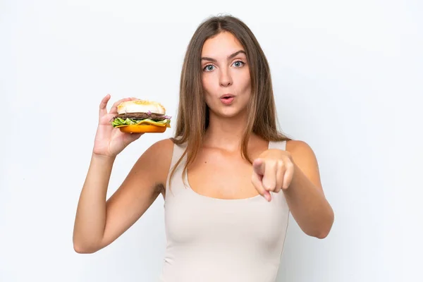 Młoda Ładna Kobieta Trzyma Hamburgera Izolowane Białym Tle Zaskoczony Wskazując — Zdjęcie stockowe
