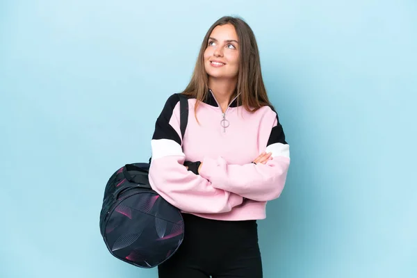 stock image Young sport woman with sport bag isolated on blue background looking up while smiling