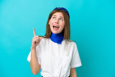 Uçak hostesi İngiliz kadın mavi arka planda izole edilmiş yukarı bakıyor ve şaşırıyor.