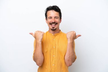 Bıyıklı genç adam beyaz arka planda izole edilmiş, baş parmakları havada ve gülümsüyor.