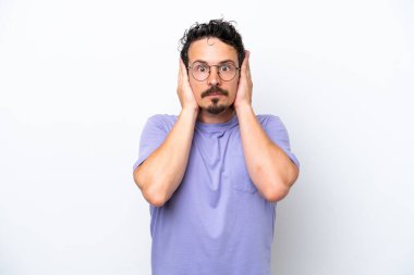 Bıyıklı genç adam beyaz arka planda izole edilmiş hayal kırıklığına uğramış ve kulaklarını kapatmış.