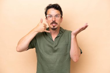Beyazlı genç bir adam bej arka planda izole edilmiş telefon jestleri yapıyor ve şüpheli.