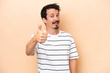 Beyaz tenli genç adam bej arka planda izole edildi. Başparmakları havada çünkü iyi bir şey oldu.