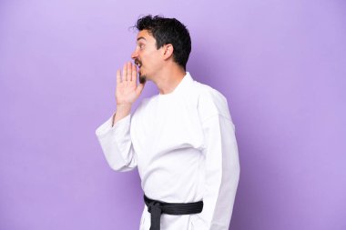 Mor arka planda karate yapan genç beyaz adam ağzı sonuna kadar açık bağırıyor.