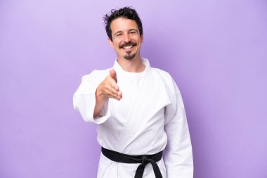 Mor arka planda karate yapan genç beyaz adam iyi bir anlaşma için el sıkışıyor.