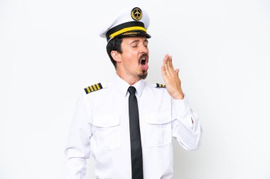 Kafkasyalı uçak pilotu beyaz arka planda izole edilmiş esniyor ve geniş ağzını eliyle kapatıyor.