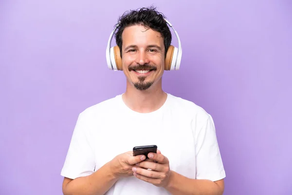 Joven Hombre Caucásico Aislado Sobre Fondo Púrpura Escuchando Música Con —  Fotos de Stock