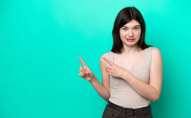 Genç Rus kadın yeşil arka planda izole edilmiş korkmuş ve kenarı işaret ediyor.