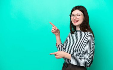 Yeşil arka planda izole edilmiş genç bir Rus kadın parmak göstererek bir ürün sunuyor.