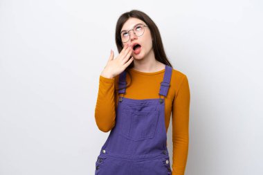 Mavi arka planda izole edilmiş genç bir Rus kadın esniyor ve elleriyle ağzını kapatıyor.