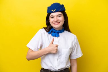 Uçak hostesi Rus kadın sarı arka planda izole edilmiş bir şekilde baş parmak hareketi yapıyor.