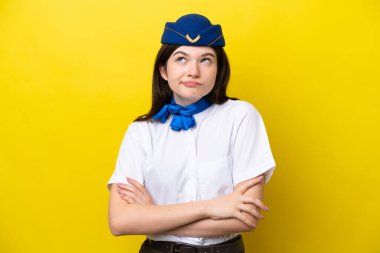 Uçak hostesi Rus kadın, sarı arka planda izole edilmiş. Omuzlarını kaldırırken şüpheyle hareket ediyor.