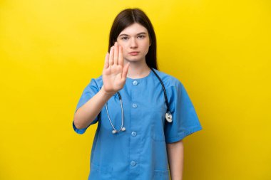 Sarı arka planda izole edilmiş genç cerrah doktor Rus kadın dur hareketi yapıyor.