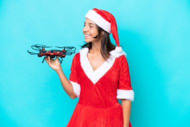 Anne Noel gibi giyinmiş genç bir kadın elinde mavi arka planda izole edilmiş bir dron tutuyor.