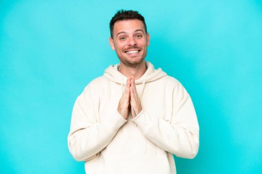 Mavi arka planda izole edilmiş beyaz tenli yakışıklı adam avuç içlerini bir arada tutuyor. İnsan bir şey ister.