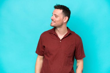 Beyaz tenli yakışıklı adam mavi arka planda izole edilmiş, yana bakıyor ve gülümsüyor.