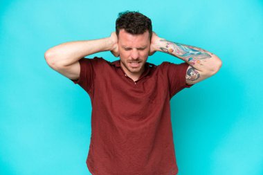 Kafkasyalı yakışıklı adam mavi arka planda izole edilmiş hayal kırıklığına uğramış ve kulaklarını kapatmış.