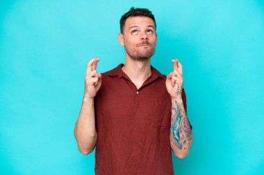 Beyaz tenli yakışıklı adam mavi arka planda izole edilmiş, şans diliyor ve en iyisini diliyor.