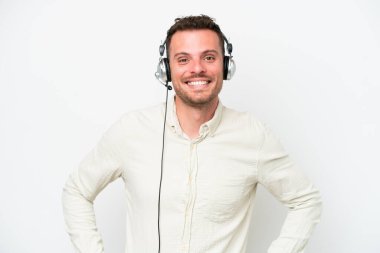 Tele pazarlamacı, beyaz arka planda izole edilmiş kulaklıkla çalışan beyaz bir adam. Kolları kalçasında ve gülümsüyor.