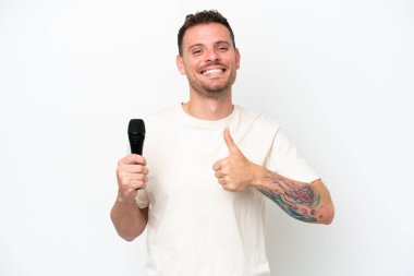 Beyaz arka planda izole edilmiş bir mikrofonu kaldıran beyaz tenli genç şarkıcı baş parmak hareketi yapıyor.