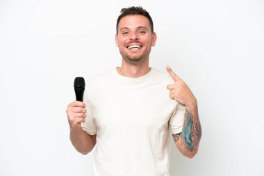 Beyaz arka planda izole edilmiş bir mikrofonu kaldıran beyaz tenli genç şarkıcı baş parmak hareketi yapıyor.