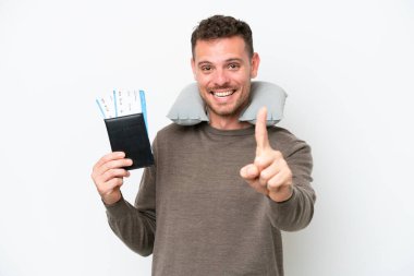 Beyaz arka planda izole edilmiş pasaport taşıyan genç beyaz bir adam parmağını kaldırıyor ve gösteriyor.