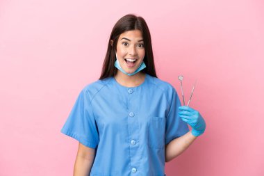Dişçi kadın, pembe arka planda sürpriz yüz ifadesiyle izole edilmiş aletler tutuyor.
