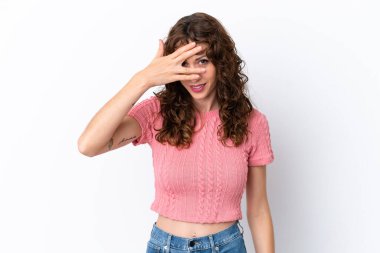 Beyaz arka planda izole edilmiş kıvırcık saçlı genç bir kadın. Gözleri elleriyle kaplıyor ve gülümsüyor.