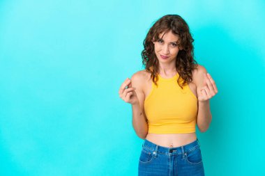Young woman with curly hair isolated on blue background making money gesture