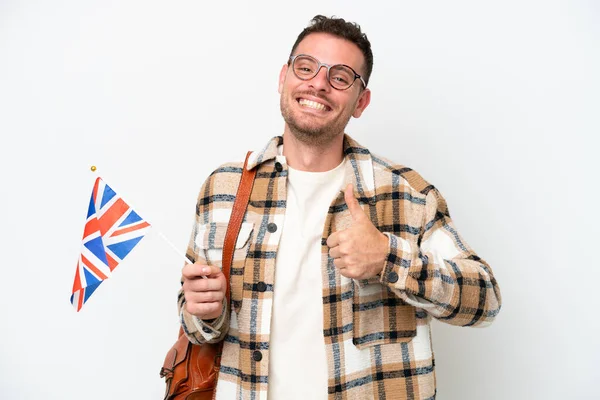 年轻的他的惊慌失措的男人举着一面英国国旗 被白色背景隔离 他举起了一个大拇指 — 图库照片