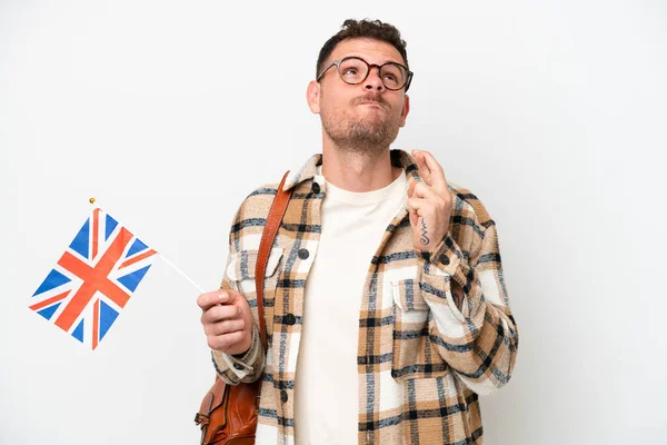年轻的他的惊慌失措的男人拿着一面英国国旗 与白色背景隔离 手指头交叉 祝愿他一切顺利 — 图库照片