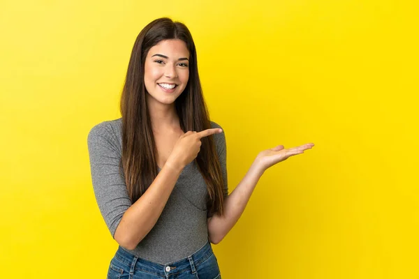 在黄色背景上被隔离的巴西年轻女子 手心上握着一个想象的复制空间 插入一个广告 — 图库照片