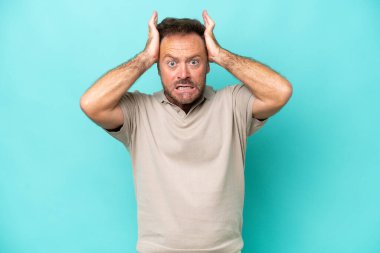 Mavi arka planda izole edilmiş orta yaşlı beyaz bir adam gergin hareketler yapıyor.